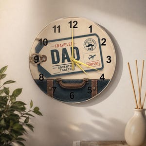 May include: A round wall clock with a vintage travel theme. The clock face features a suitcase design with the word "DAD" and the text "World's Best Dad". The clock has black numbers and yellow hands.