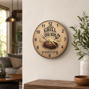 Peut inclure: Une horloge murale ronde au cadran beige ornée d'un steak grillé, d'une fourchette et d'une spatule. Le texte indique Grill Smoke & Steak Master Dial, Est 2024, et Happy Father's Day Best Dad Ever. Elle possède des chiffres noirs et des aiguilles dorées.