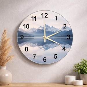 Op de afbeelding: Ronde wandklok met een berg- en meerlandschap. De wijzerplaat heeft zwarte cijfers en lichtgekleurde wijzers. De achtergrond toont de weerspiegeling van de bergen in het water. Een decoratief item voor in huis.