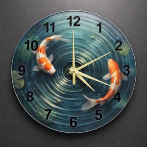 May include: Round wall clock featuring a koi fish design. The clock face has a blue water background with two orange and white koi fish. The clock hands are a light yellow color, and the numbers are black.
