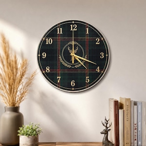 May include: Round wall clock with a green and red plaid pattern. The clock face features gold-colored numerals and hands, with a central emblem of a deer head within a wreath. The clock is mounted on a light-colored wall.