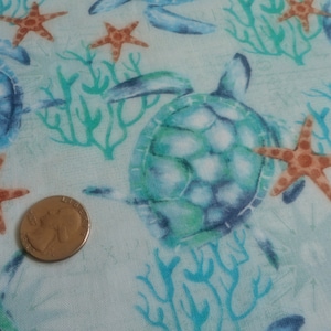 May include: Fabric with a repeating pattern of sea turtles, starfish, and coral in shades of blue, green, and orange on a light blue background. A US quarter coin is included for scale.