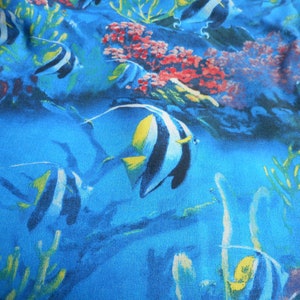 May include: A blue fabric with a colorful print of tropical fish and coral reefs. The fish are black, white, and yellow with a blue background.