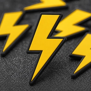 May include: Close-up of several yellow lightning bolt-shaped objects with black borders. The bolts are arranged on a textured, dark gray surface. The bright yellow color of the bolts contrasts with the dark background, creating a bold visual.