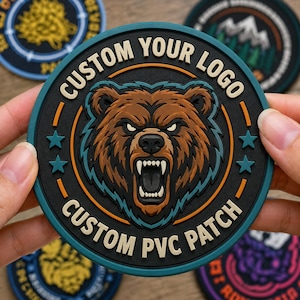 May include: A round, black PVC patch with a brown bear illustration. The bear has an open mouth with visible teeth. The text "CUSTOM YOUR LOGO" and "CUSTOM PVC PATCH" are in white. Teal stars and accents surround the bear.