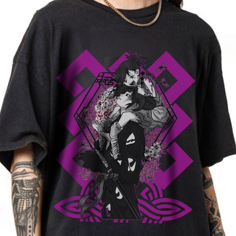 Op de afbeelding: Donkergrijs T-shirt met een zwart-wit anime-stijl illustratie van twee figuren, waarvan &eacute;&eacute;n de ander draagt. Het ontwerp bevat een paarse geometrische achtergrond met bloemaccenten. Een gouden ketting is zichtbaar aan de bovenkant.