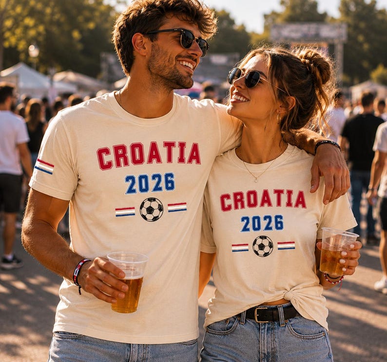 Puede incluir: Dos camisetas de manga corta color crema con el texto rojo CROATIA, el texto azul 2026, un gr&aacute;fico de bal&oacute;n de f&uacute;tbol en blanco y negro, y peque&ntilde;as rayas horizontales rojas, blancas y azules en la parte frontal.