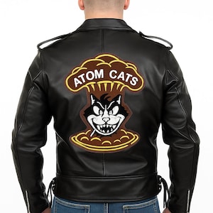 Può includere: Giacca in pelle nera con una grande toppa "ATOM CATS" sul retro. La toppa presenta un gatto dei cartoni animati con una sigaretta, su uno sfondo a forma di fungo atomico marrone. La giacca ha un classico stile motociclista con cerniere e cinturini.