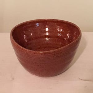 May include: A red ceramic bowl with a slightly uneven rim and a speckled glaze.