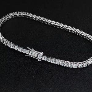 Peut inclure: Un bracelet de tennis argenté orné d'une rangée de pierres précieuses claires et étincelantes. Le bracelet est en métal argenté et possède un fermoir sécurisé. Les pierres précieuses sont espacées uniformément et reflètent la lumière.