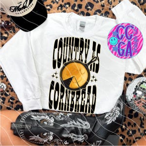 Puede incluir: Sudadera blanca con el texto negro "COUNTRY AS CORNBREAD", con una sartén con pan de maíz. También se ven una gorra de béisbol en blanco y negro y botas de vaquero negras.