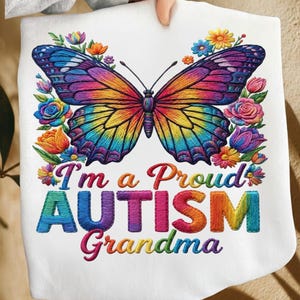 May include: White sweatshirt featuring a colorful butterfly design with a rainbow of colors. The text "I'm a Proud AUTISM Grandma" is embroidered below the butterfly, surrounded by floral accents.