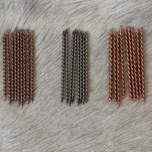 May include: Three distinct groups of thin, pointed metal rods arranged in vertical rows. The left group features copper and dark metal twisted rods, the center group contains dark grey twisted rods, and the right group consists of copper-colored twisted rods.