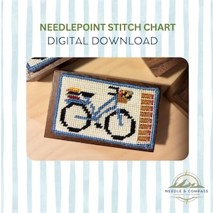 May include: A needlepoint stitch chart digital download featuring a stitched design of a light blue bicycle with black wheels, a colorful basket, and a rear rack. The rectangular needlepoint piece is mounted on a dark wood block frame.