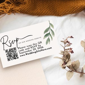 Peut inclure: Une carte RSVP crème avec une écriture noire élégante et un code QR. La carte contient le texte "ON OUR WEDDING WEBSITE" et les instructions pour répondre avant le 29 septembre 2026, avec une adresse de site web. Des feuilles vertes à l'aquarelle ornent le coin supérieur droit.