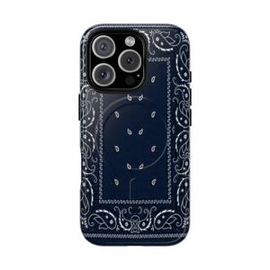 May include: A dark navy blue phone case featuring a white paisley bandana pattern. The design includes a central rectangular border with intricate floral motifs and a circular magnetic charging ring visible on the back of the protective cover.