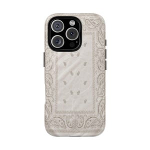 Può includere: Una custodia per smartphone con stampa bandana color beige chiaro e bianco sporco, caratterizzata da intricati motivi paisley e un bordo rettangolare centrale. La custodia presenta un modulo fotocamera nero con tre obiettivi.
