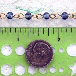 May include: A close-up of a chain of dark blue glass beads with gold metal links. The chain is measured against a ruler and a US dime for scale.