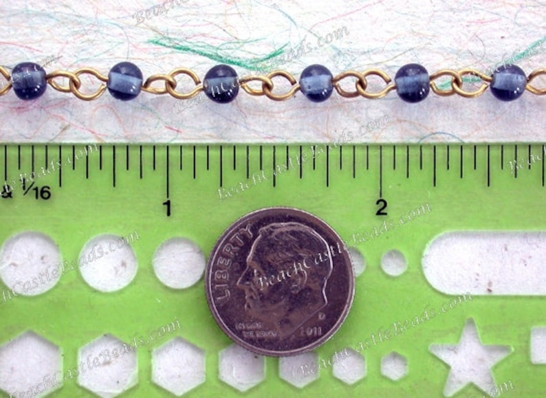 May include: A close-up of a chain of dark blue glass beads with gold metal links. The chain is measured against a ruler and a US dime for scale.