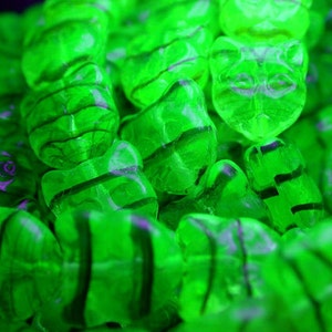 May include: A close-up of a pile of green gummy candies shaped like bears. The candies have a striped pattern and are arranged in a random order.