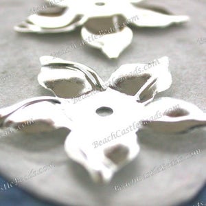 以下が含まれることがあります： 銀色の金属製のフラワーシェイプの装飾品が2つ。花は5枚の花びらと中央に穴があります。