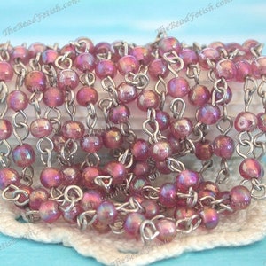 May include: A strand of iridescent pink glass beads strung on a silver chain. The beads are small and round, and the chain is delicate.