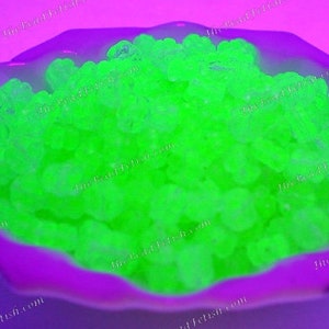 May include: A close-up of a bowl filled with bright green glow-in-the-dark beads. The beads are small and round, and they are arranged in a random pattern. The bowl is made of a purple material and has a smooth, glossy finish.