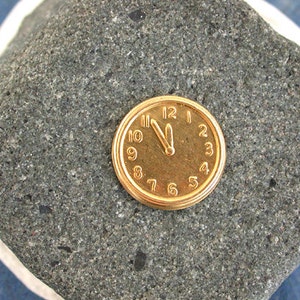 May include: A gold-coloured pocket watch with Roman numeral markings on a grey stone background.