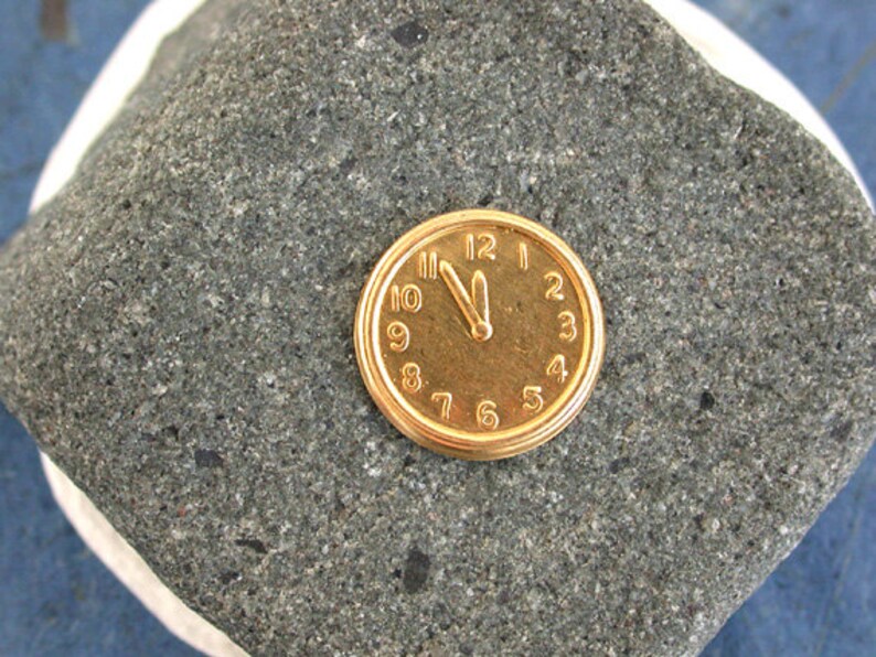 May include: A gold-coloured pocket watch with Roman numeral markings on a grey stone background.
