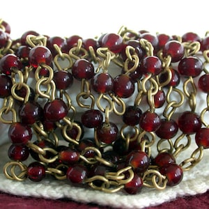 May include: A close-up of a long chain necklace made of small, round, dark red glass beads and gold metal chain links.