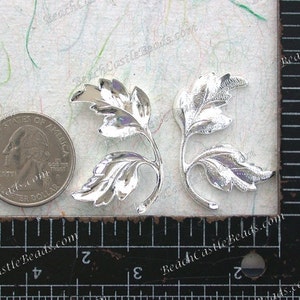 Puede incluir: Dos adornos met&aacute;licos en forma de hoja plateados con un acabado texturizado. Los adornos miden aproximadamente 2,5 cm de largo y se muestran junto a una moneda de veinticinco centavos de d&oacute;lar estadounidense para comparar el tama&ntilde;o.