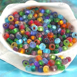 May include: A collection of colorful glass beads in various shades of red, green, blue, orange, and purple. The beads are inside a white seashell, with some beads spilling out. The image has a soft focus and a bright, cheerful feel.