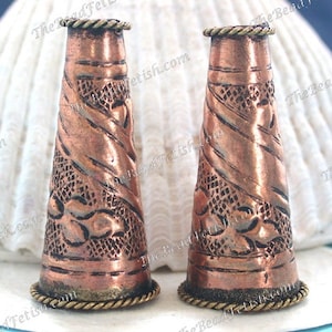 May include: Two copper thimbles with a decorative embossed design. The thimbles have a gold-coloured band around the top and bottom.