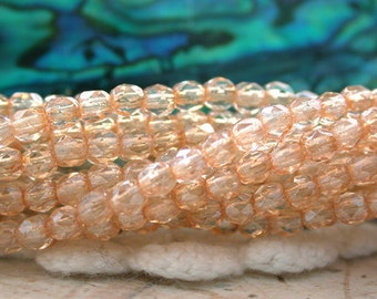 May include: A strand of peach-colored glass beads with a faceted, iridescent finish. The beads are round and have a slight shimmer.