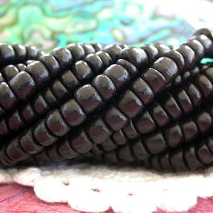 May include: A strand of black wooden beads, arranged in a woven pattern. The beads are smooth and glossy, creating a sleek and elegant look.