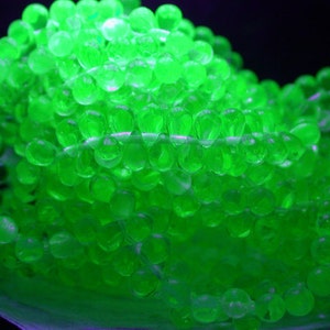 May include: Close-up of a strand of glowing green beads. The beads are round and translucent, with a bright, neon-like appearance. The beads are strung together, creating a necklace or bracelet.