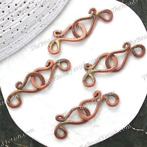 May include: Four copper wire clasps with a decorative swirl design. The clasps are on a white surface.