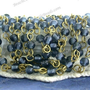 May include: A strand of blue glass beads strung on a gold chain. The beads are round and have a slightly frosted finish. The chain is made of small, linked rings.
