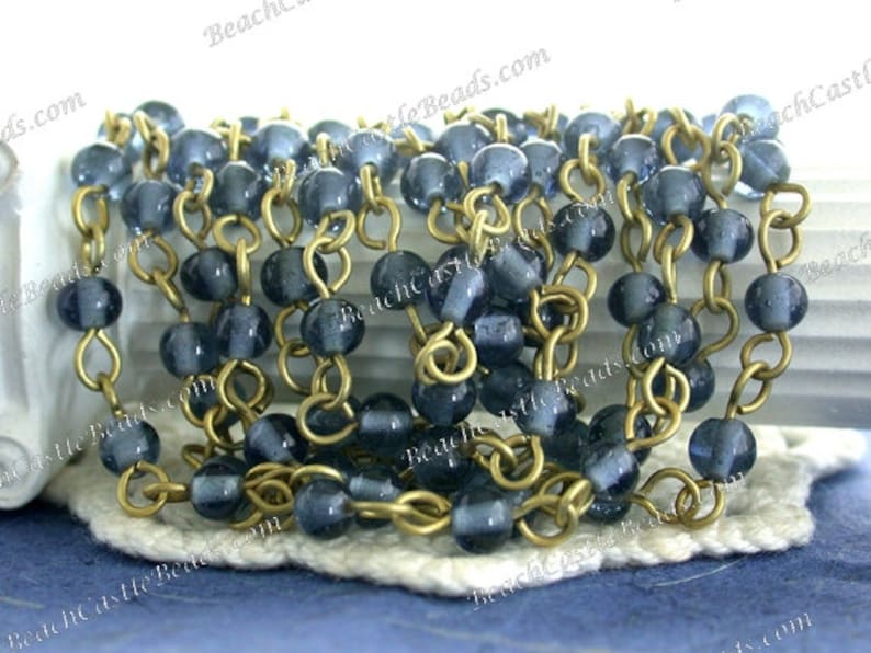 May include: A strand of blue glass beads strung on a gold chain. The beads are round and have a slightly frosted finish. The chain is made of small, linked rings.