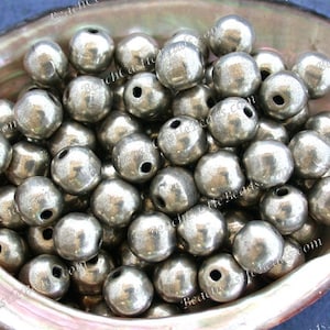 May include: A close-up of a pile of silver metal beads. The beads are round and have a slightly textured surface. They are all about the same size and are arranged in a random pattern.
