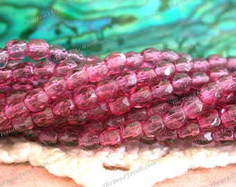 May include: A strand of pink glass beads with a faceted finish. The beads are small and round, and they have a translucent appearance.
