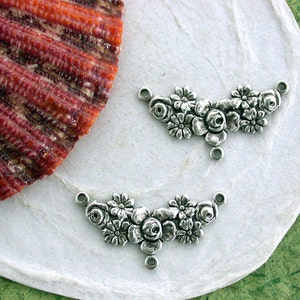 May include: Two silver-toned metal floral embellishments with three loops for attaching to jewelry or other crafts. Each embellishment features a cluster of raised roses and smaller flowers.