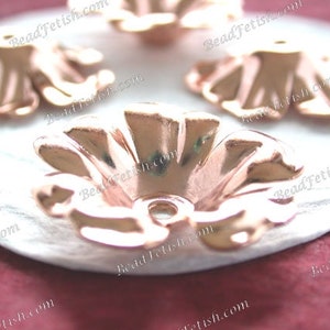 May include: Five rose gold metal flower-shaped embellishments with a hole in the center. The embellishments are on a white surface.