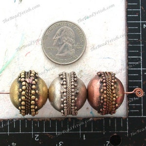 May include: Three round beads with a metallic finish. The beads are made of metal and have a textured surface. The beads are gold, silver, and copper in color. The beads are approximately 1 inch in diameter.