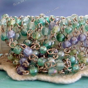 May include: A silver chain necklace with green and purple iridescent glass beads. The beads are strung on a silver chain and have a shiny finish.