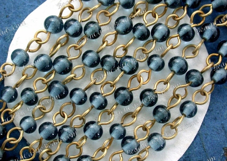 May include: A strand of dark blue glass beads strung on a gold chain. The beads are round and have a slightly textured surface.
