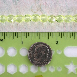 Puede incluir: Una hebra de cuentas de vidrio facetadas de color verde lima, de aproximadamente 1,25 cm de di&aacute;metro, medidas con una regla y una moneda de diez centavos de d&oacute;lar estadounidense.