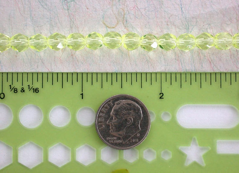 Puede incluir: Una hebra de cuentas de vidrio facetadas de color verde lima, de aproximadamente 1,25 cm de di&aacute;metro, medidas con una regla y una moneda de diez centavos de d&oacute;lar estadounidense.