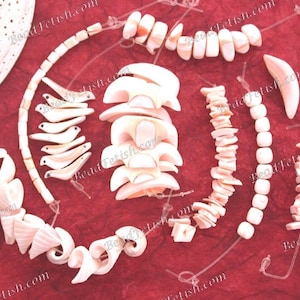 May include: A collection of natural shell beads and components in diverse shapes, such as spirals, curved pieces, and rectangular beads. The beads are mainly white and pale pink, displayed on a deep red surface.