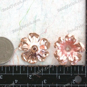May include: Two rose gold metal flower embellishments, each with five petals and a hole in the center. The flowers are approximately 1 inch in diameter and are shown next to a ruler.
